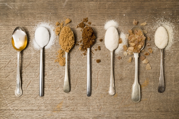 Seven teaspoons of assorted sugar spilling onto a wooden background